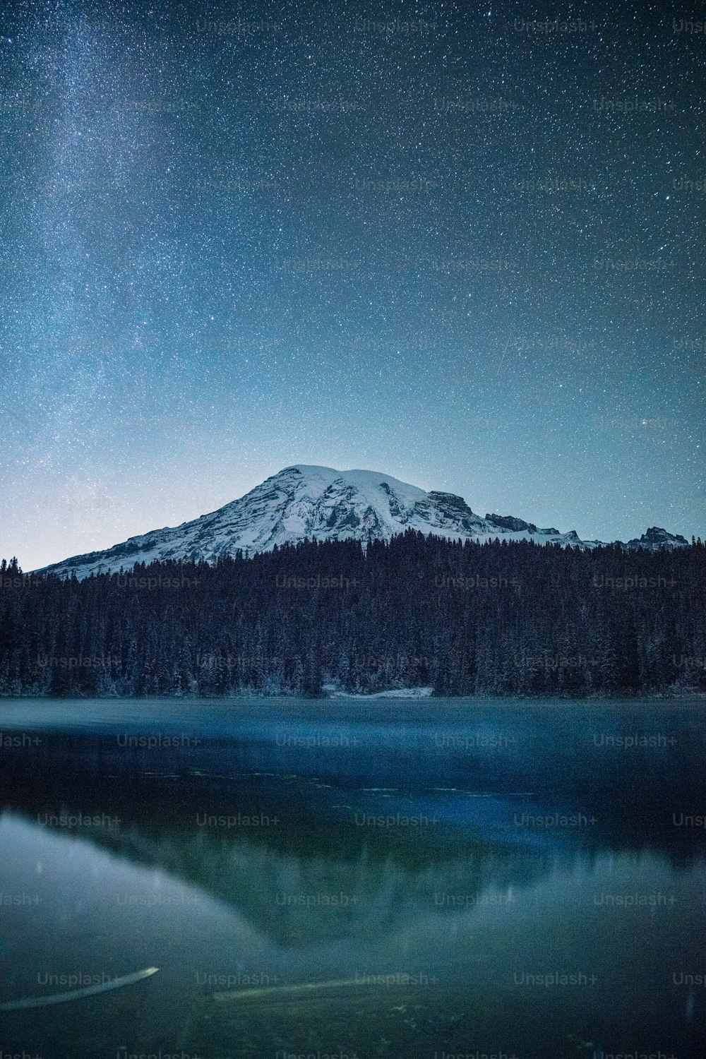 une montagne avec un lac devant elle sous un ciel nocturne