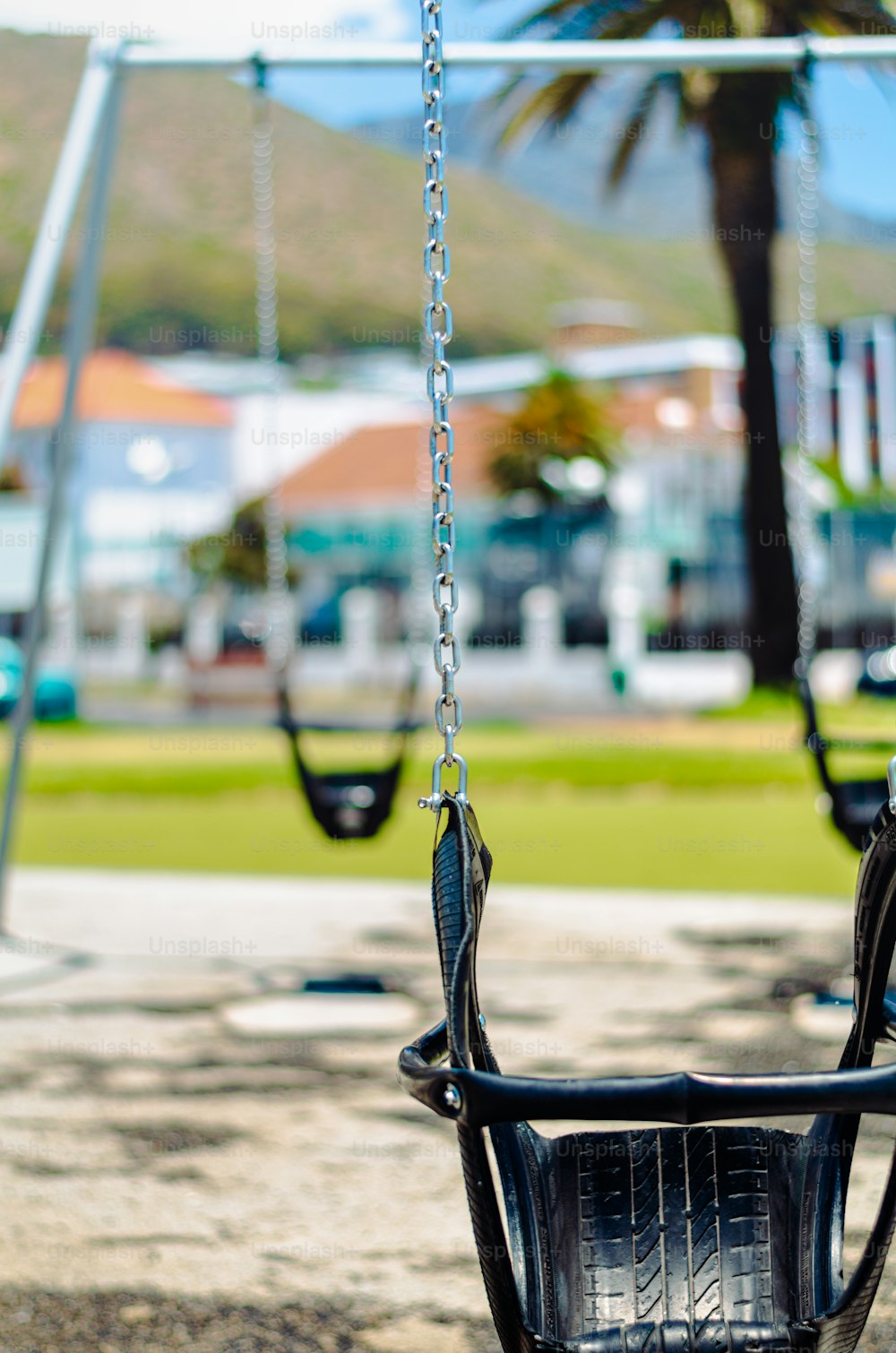 a black swing set in a park with a palm tree in the background