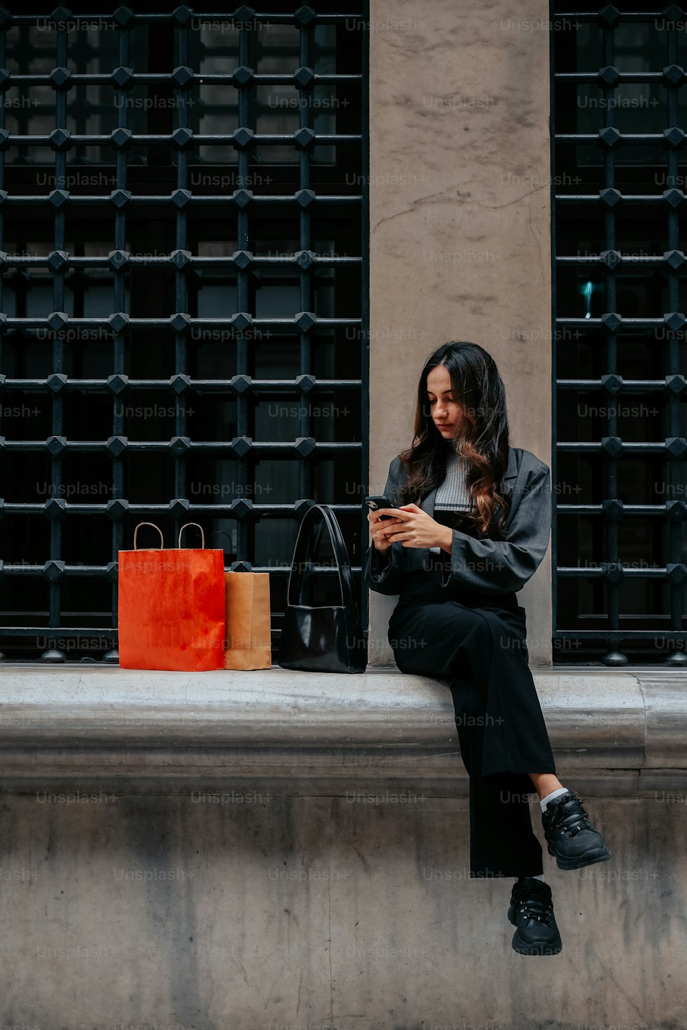 Una mujer sentada en una repisa mirando su teléfono celular