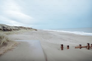 a sandy beach next to the ocean with a wooden fence