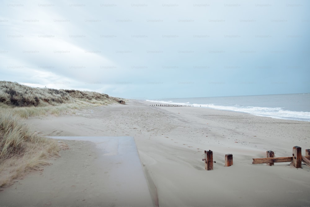 a sandy beach next to the ocean with a wooden fence