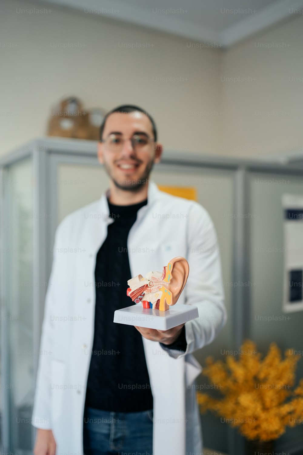 a man in a lab coat holding a model of a human ear