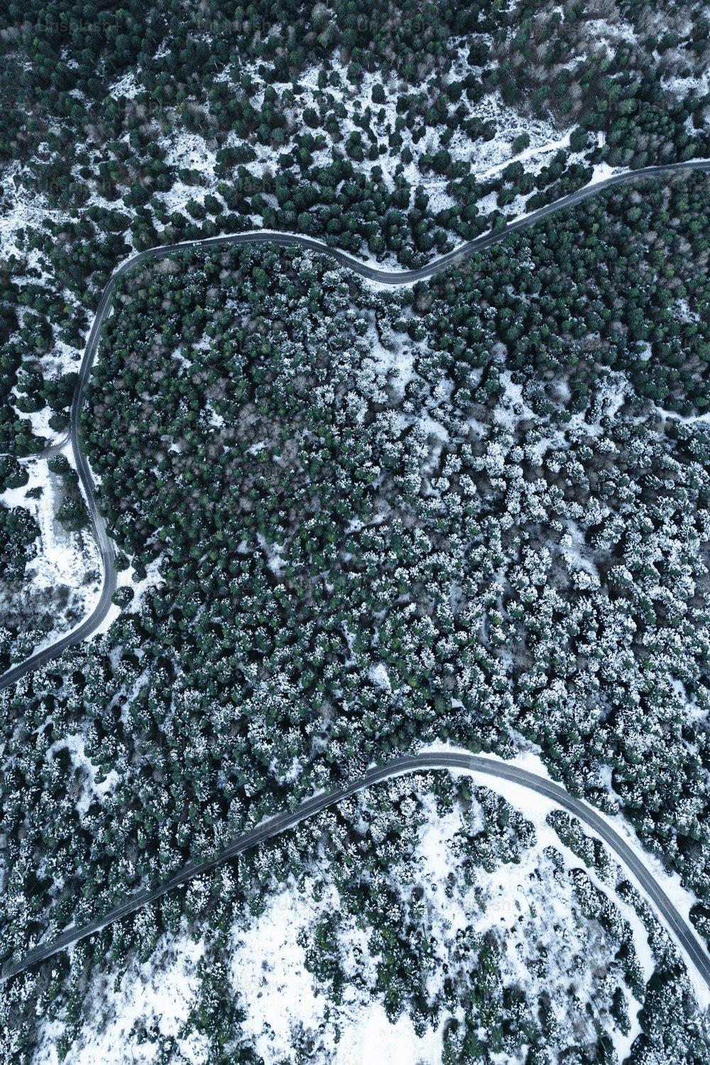 an aerial view of a road winding through a snow covered forest