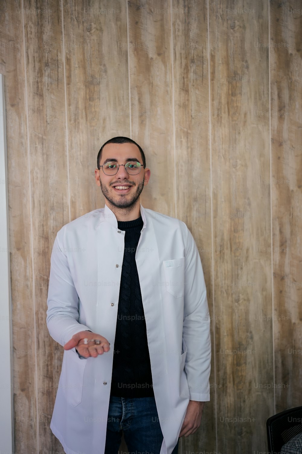 a man in a lab coat and tie standing in front of a wooden wall