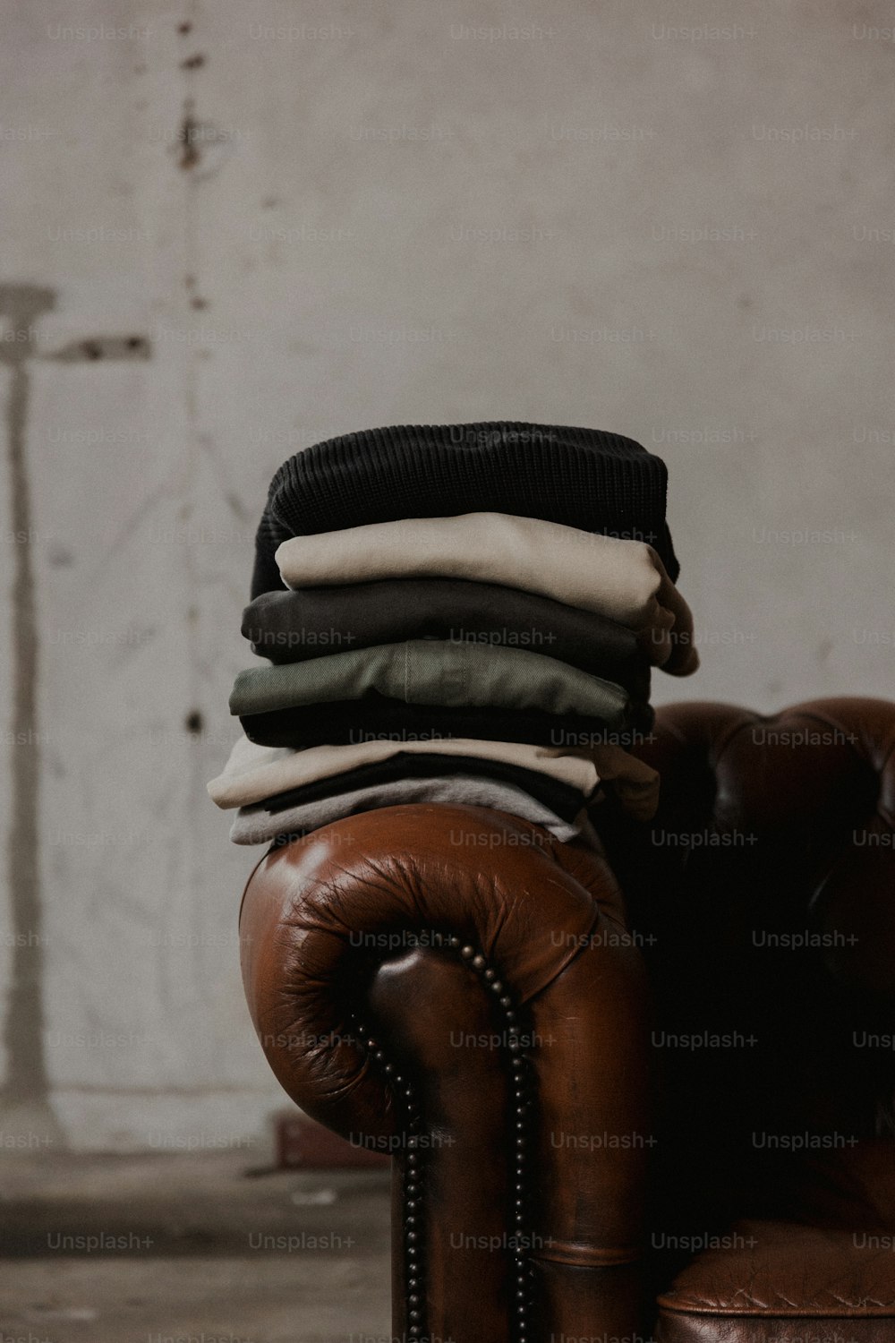uma pilha de roupas sentada em cima de uma cadeira de couro marrom