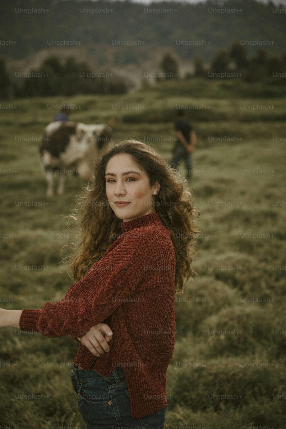 uma mulher em pé em um campo ao lado de uma vaca