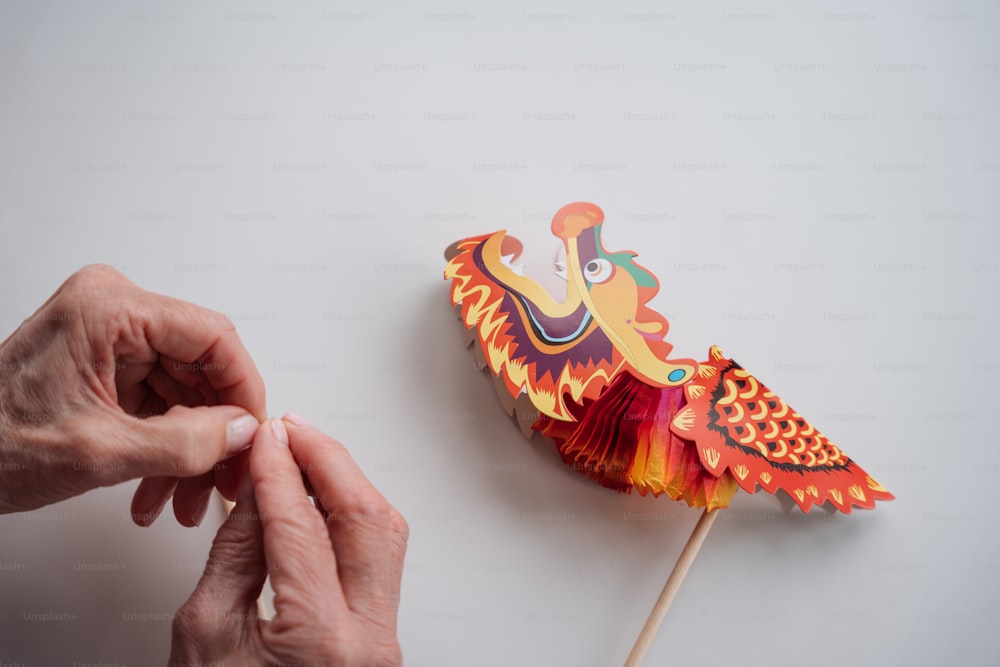 a person holding a colorful paper bird on a stick