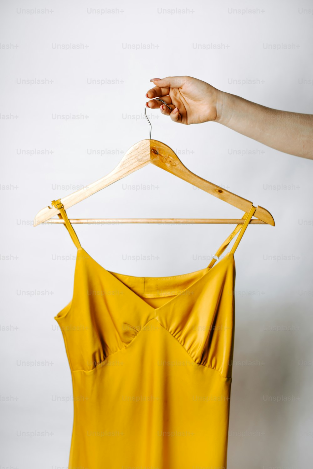 Die Hand einer Frau, die ein gelbes Oberteil auf einem Kleiderbügel hält