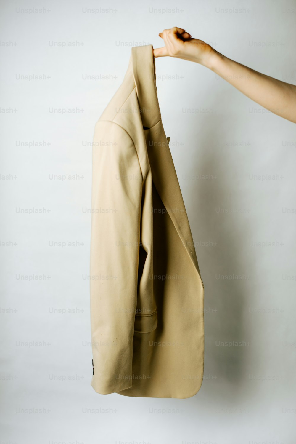 a person holding a beige jacket on a hanger