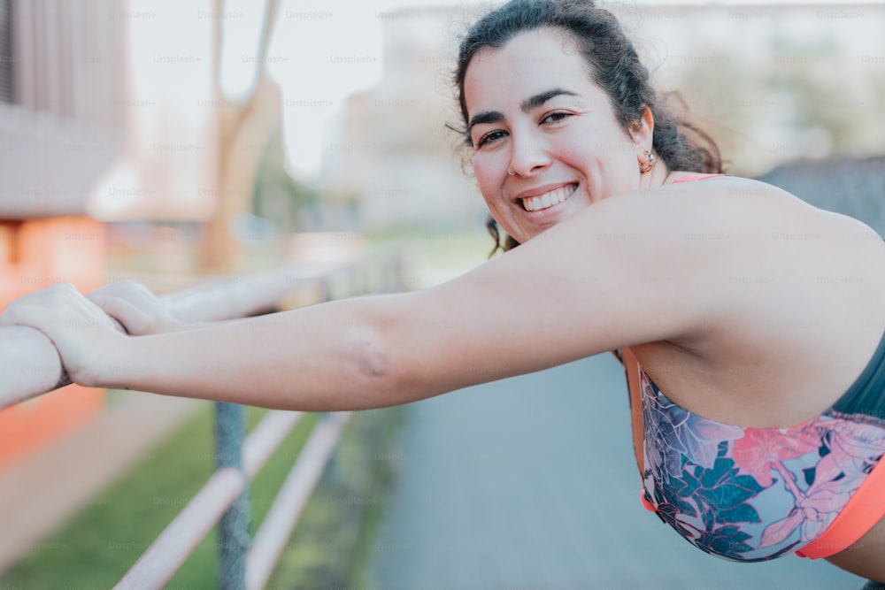 a woman in a sports bra smiling and leaning on a fence