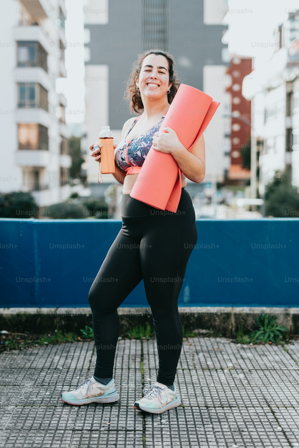 a woman is holding a yoga mat and a cup