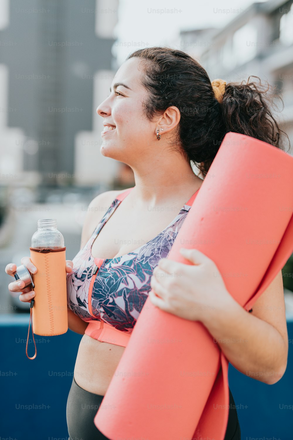 Una mujer sosteniendo una botella de agua y una esterilla de yoga