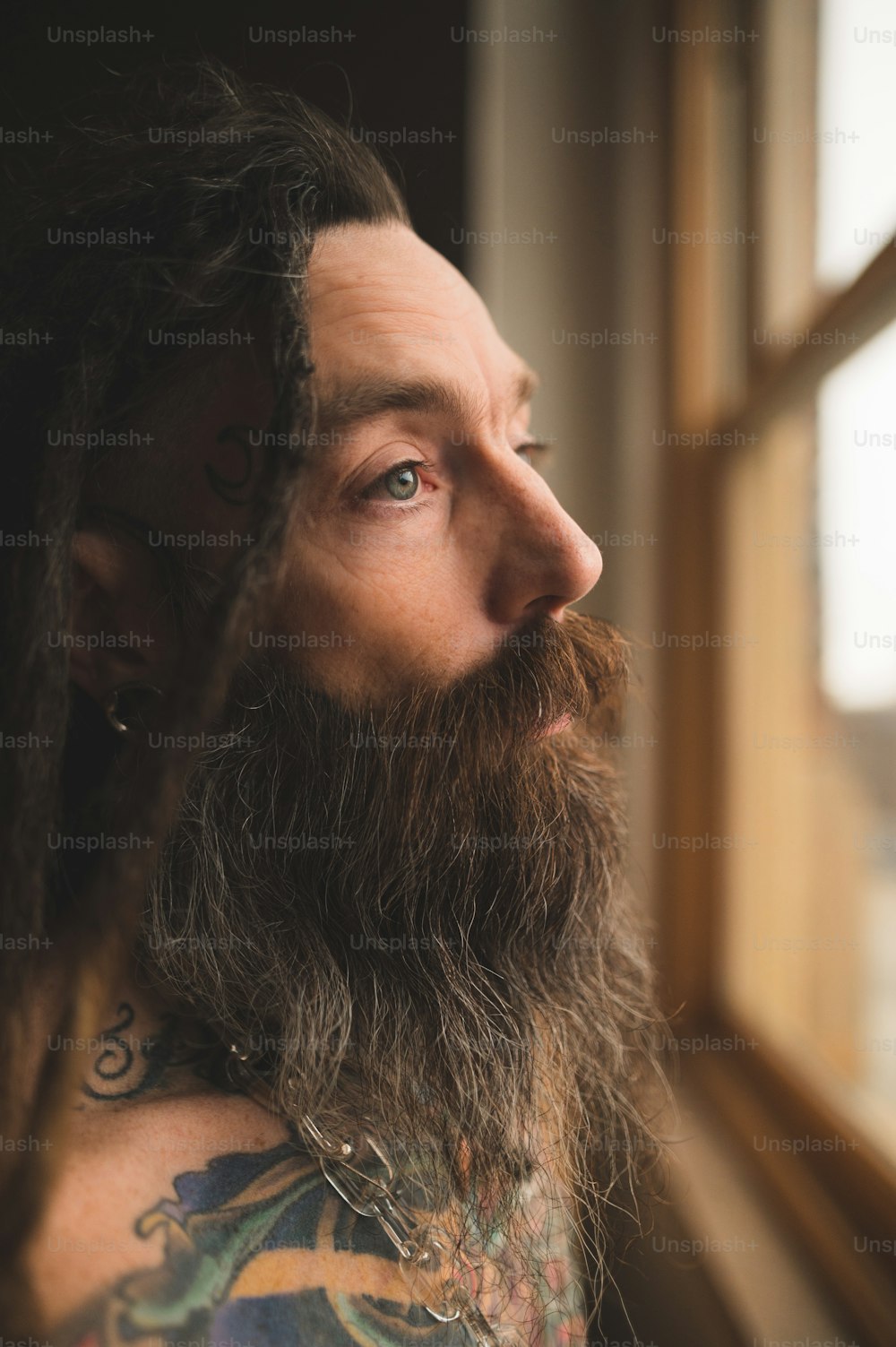 a man with long hair and a beard looking out a window