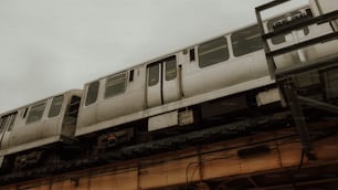 a silver train traveling over a bridge under a cloudy sky