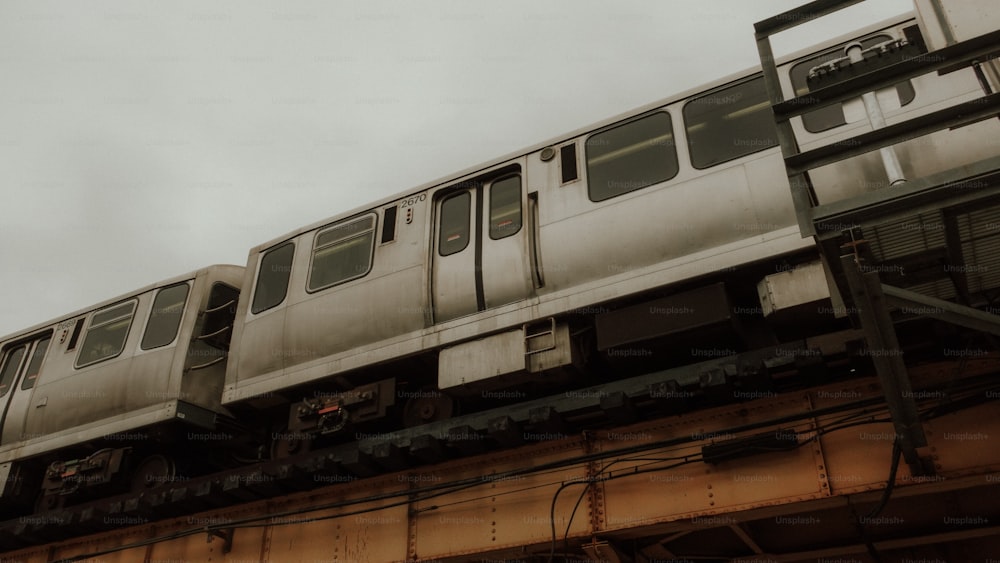 a silver train traveling over a bridge under a cloudy sky