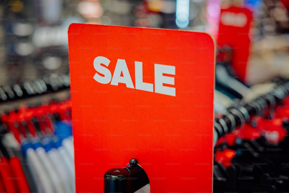 Un letrero rojo de venta sentado encima de un estante de ropa