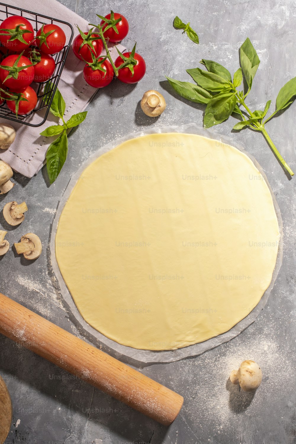 a pizza dough on a table with tomatoes, mushrooms, and a rolling pin