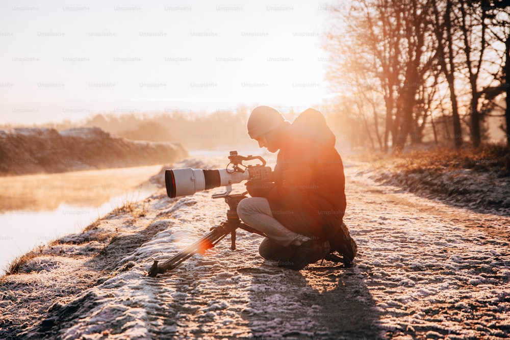 Un uomo inginocchiato vicino a un fiume con una macchina fotografica