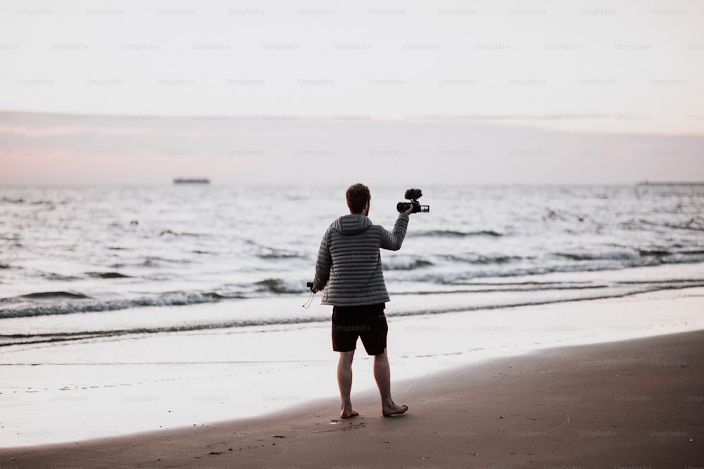 Un hombre parado en la cima de una playa sosteniendo una cámara