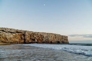 a beach with waves coming in to the shore and a rock outcropping