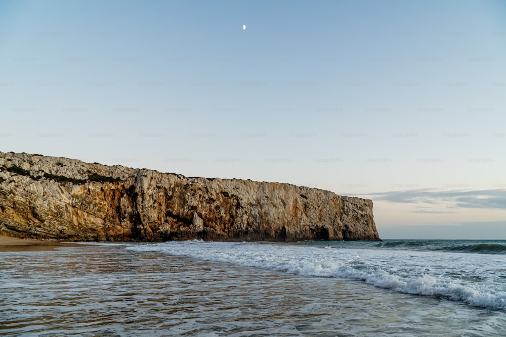 a beach with waves coming in to the shore and a rock outcropping