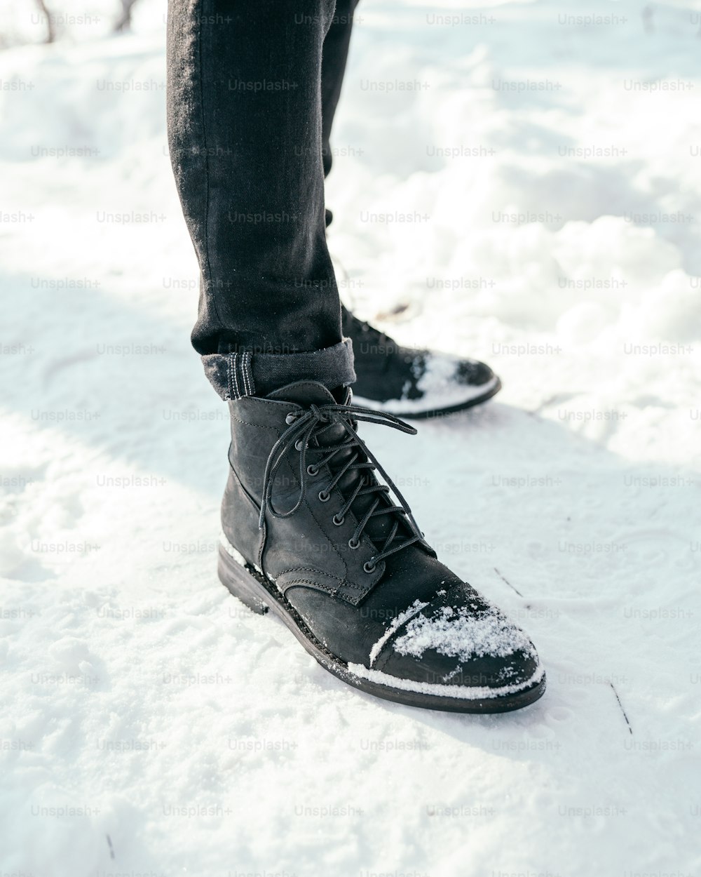 Eine Person, die mit einem Paar schwarzer Schuhe im Schnee steht