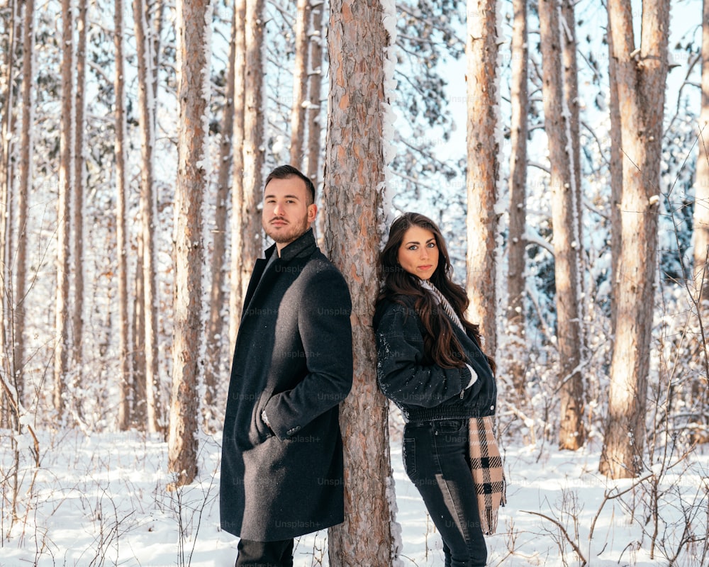um homem e uma mulher de pé ao lado de uma árvore na neve