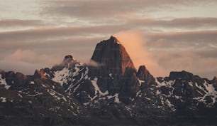 a very tall mountain covered in snow under a cloudy sky