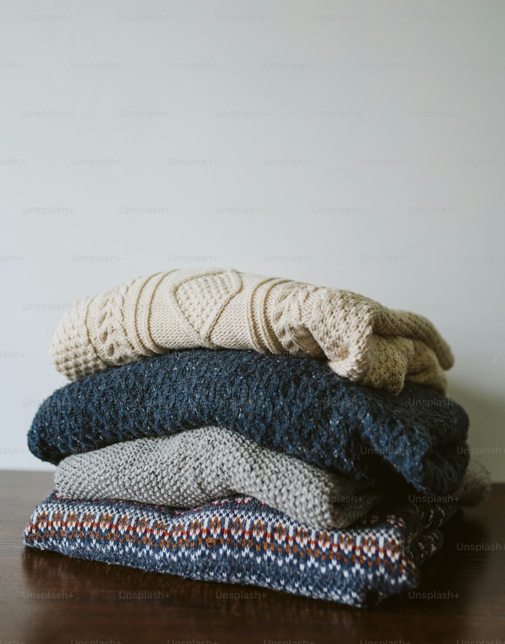 a stack of folded sweaters sitting on top of a wooden table