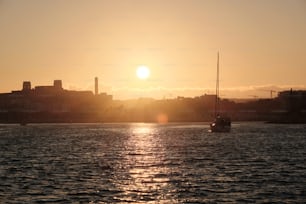 Die Sonne geht über dem Wasser unter, im Vordergrund ein Segelboot