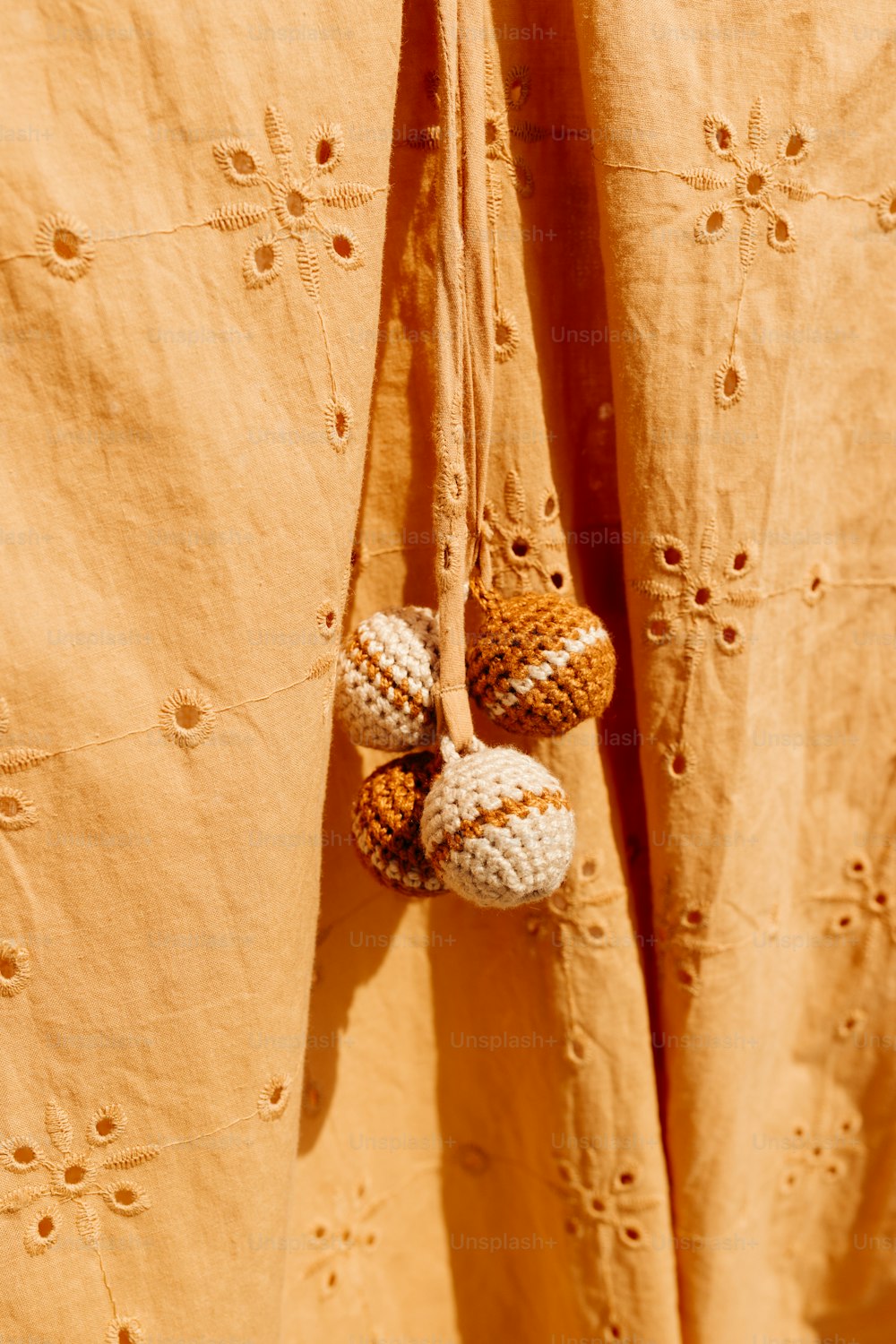 a pair of crocheted balls hanging from a curtain