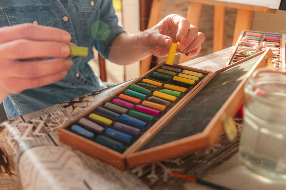 a person holding a pencil in front of a box of crayons