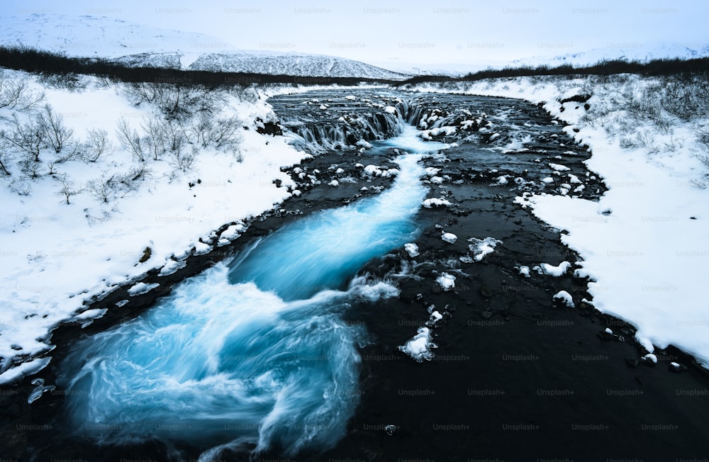 um fluxo de água que corre através de uma paisagem coberta de neve