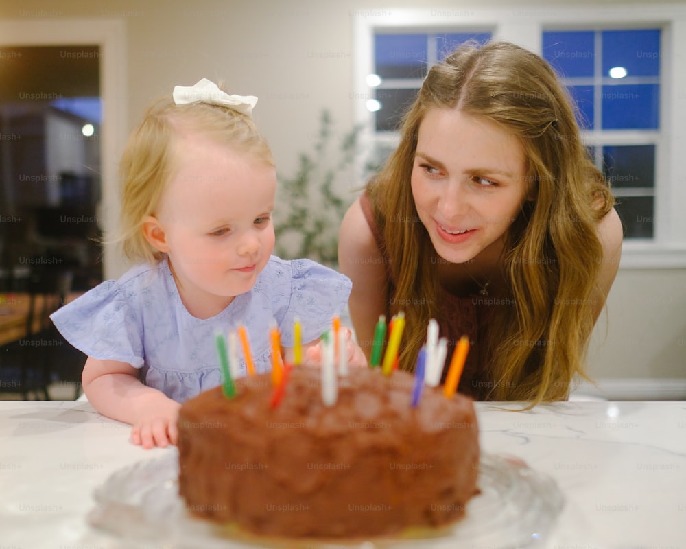uma mulher e uma menina olhando para um bolo de chocolate com velas acesas
