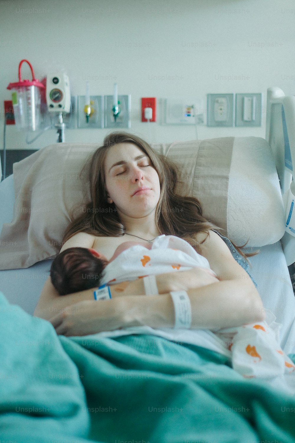 病院のベッドに横たわって赤ん坊を抱え�る女性
