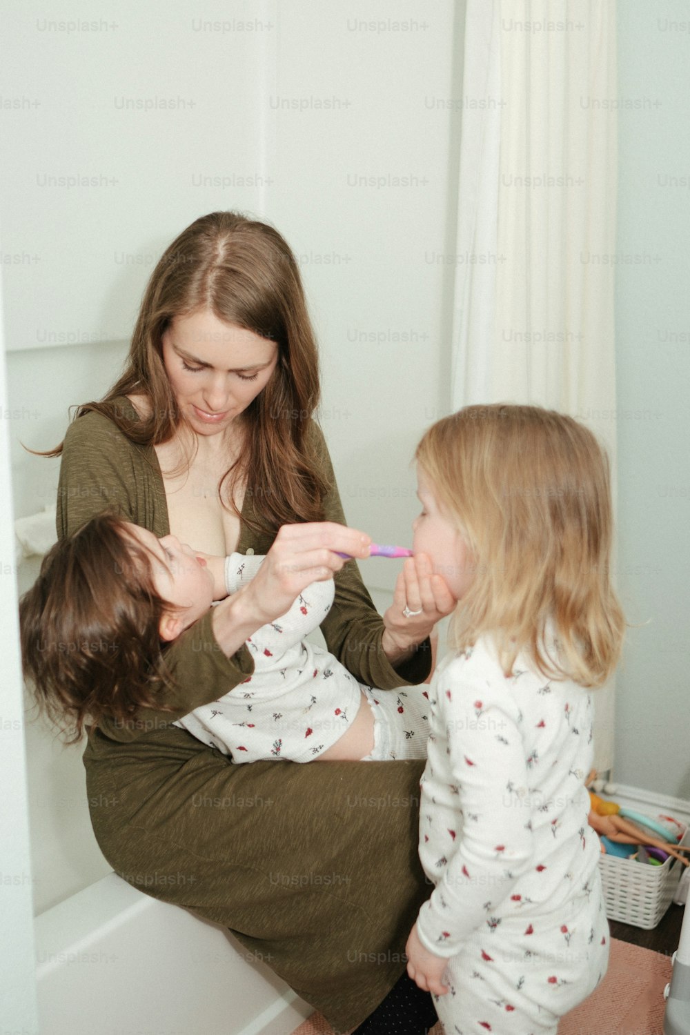 a woman brushing her teeth with two small children