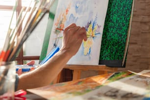 a person holding a paintbrush in front of a painting on a easel