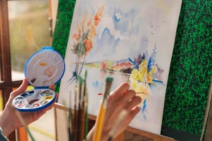 Una persona sosteniendo un pincel y una paleta frente a una pintura