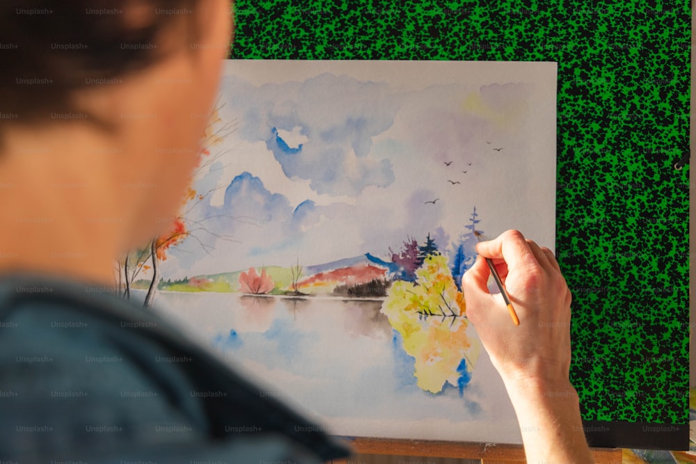 a woman is painting a landscape with watercolors