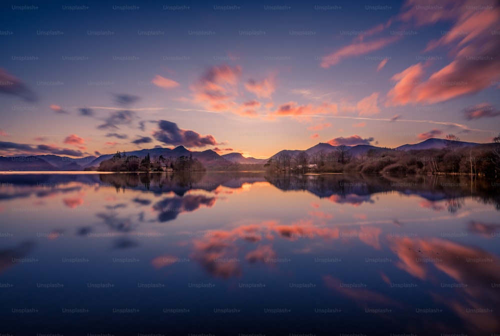 Il sole sta tramontando su un lago con le montagne sullo sfondo