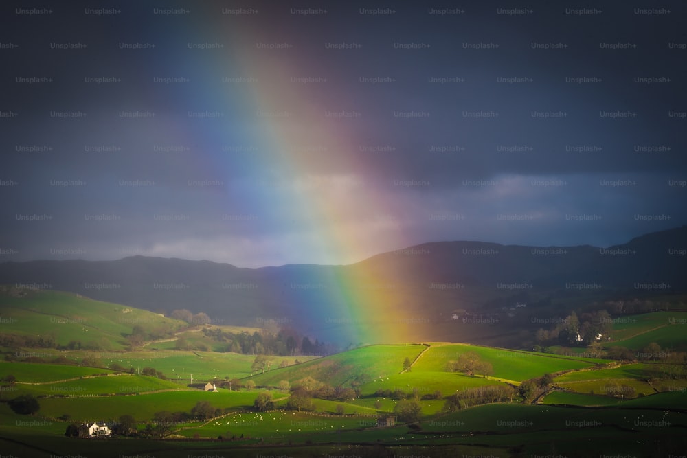 a rainbow shines in the sky over a green valley