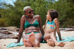 a woman sitting next to a little girl on a beach