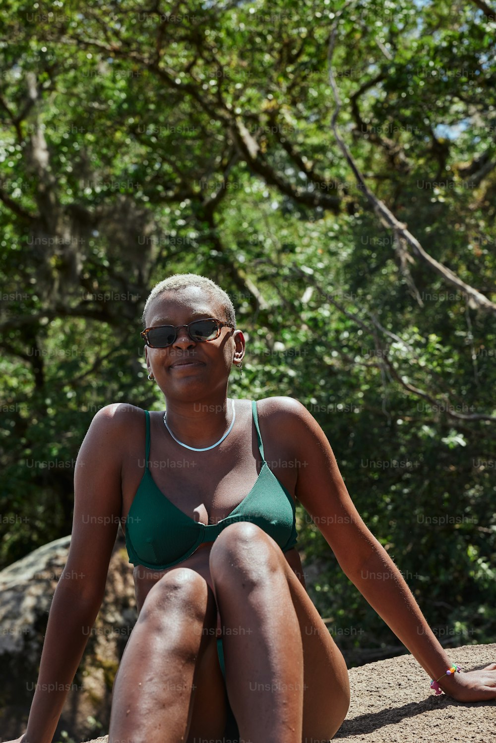 a woman in a green bikini sitting on a rock
