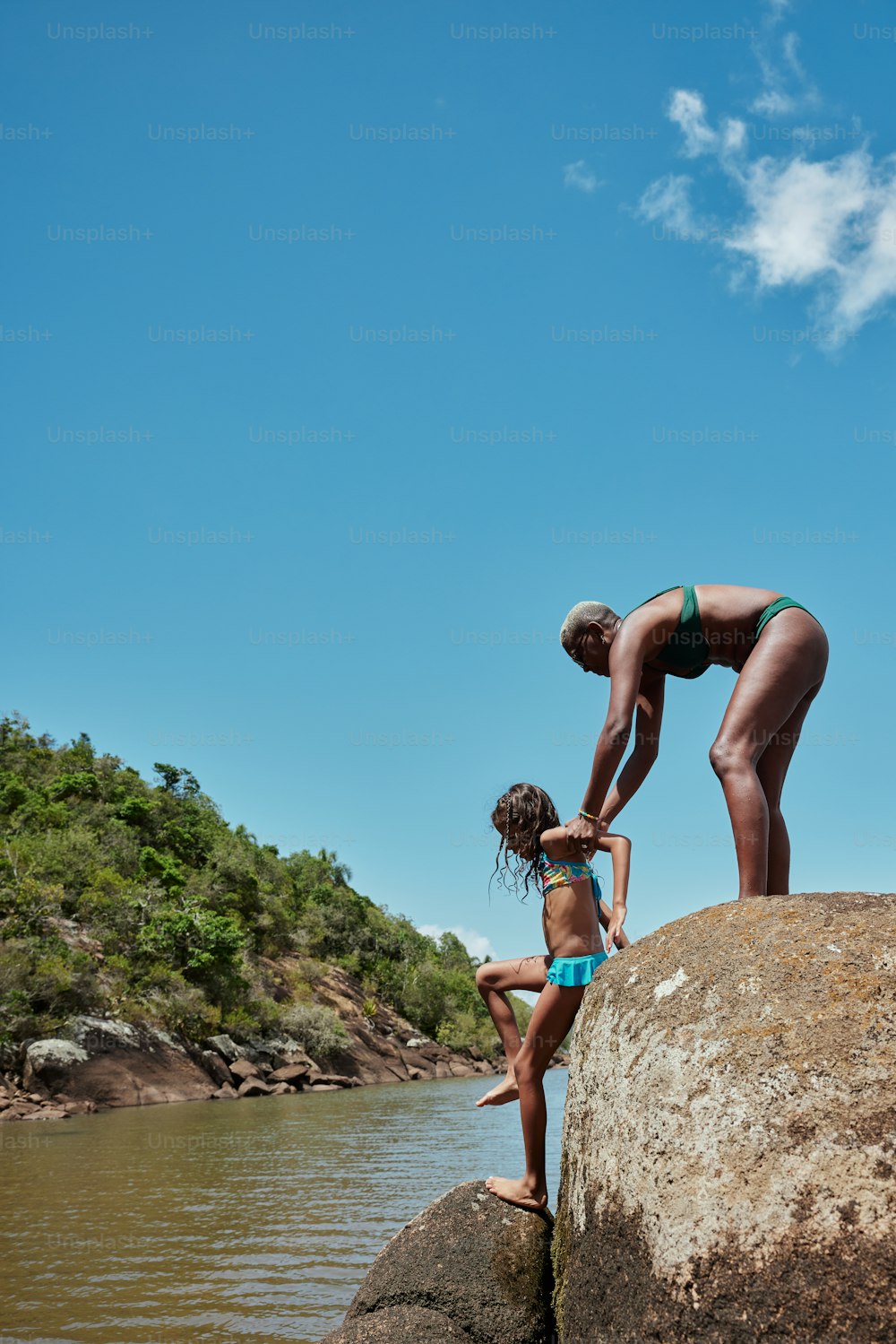 a woman and a child standing on a rock by a body of water