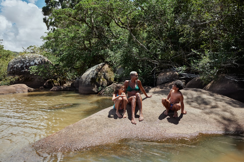 a group of people sitting on top of a rock next to a river