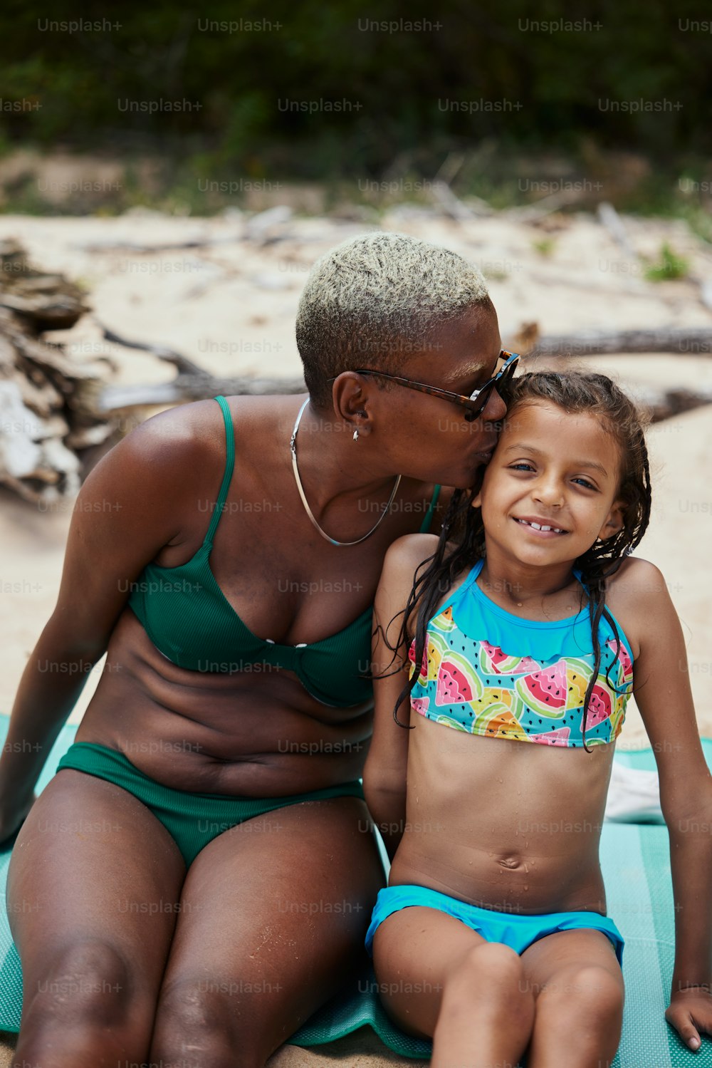 a woman sitting next to a little girl on a beach