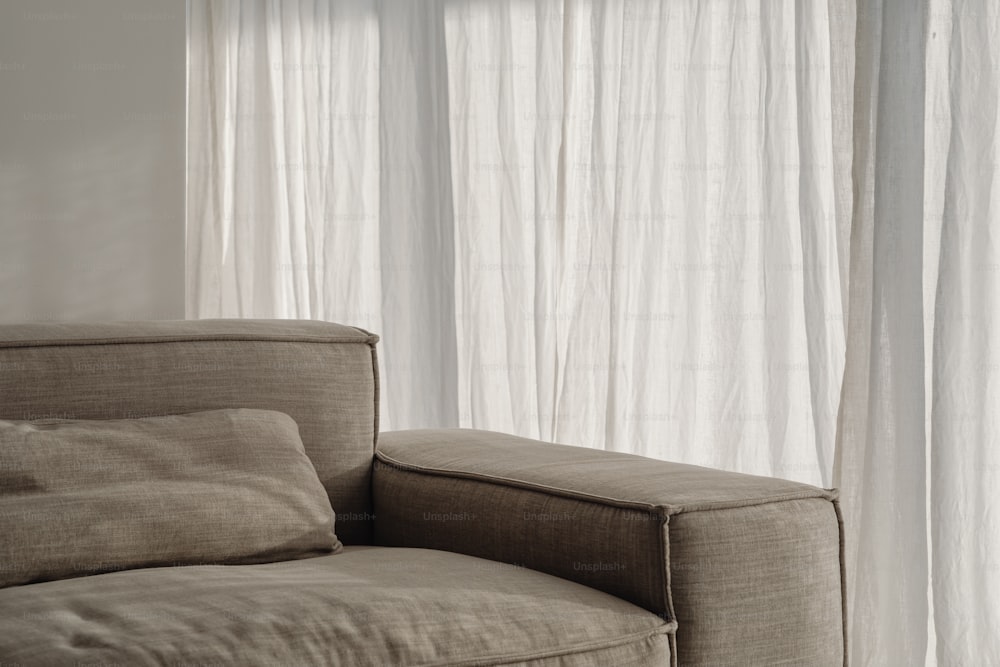um sofá sentado em frente a uma janela com cortinas brancas