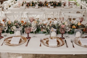 a table set for a formal dinner with flowers and greenery