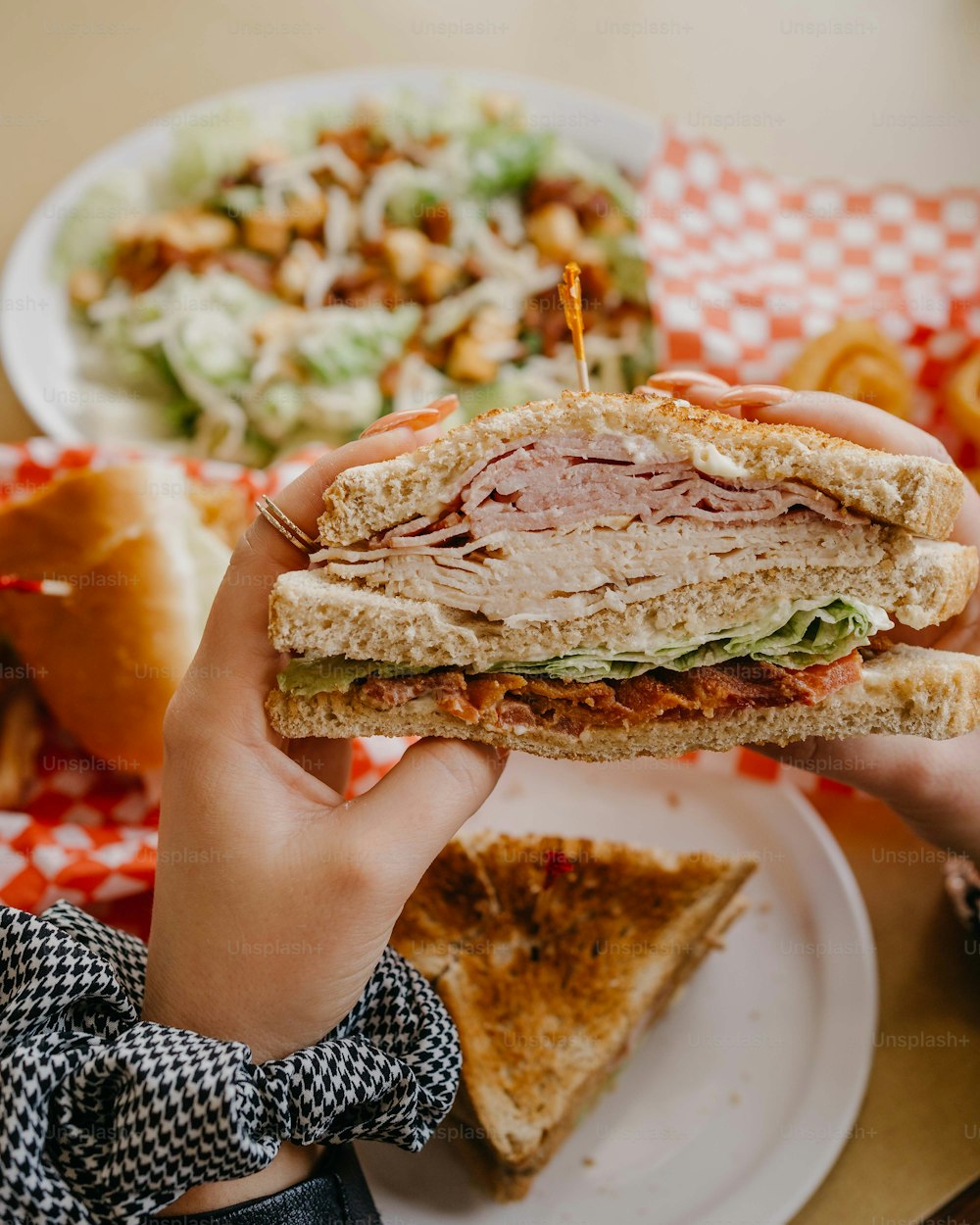 a person holding a sandwich over a plate of food