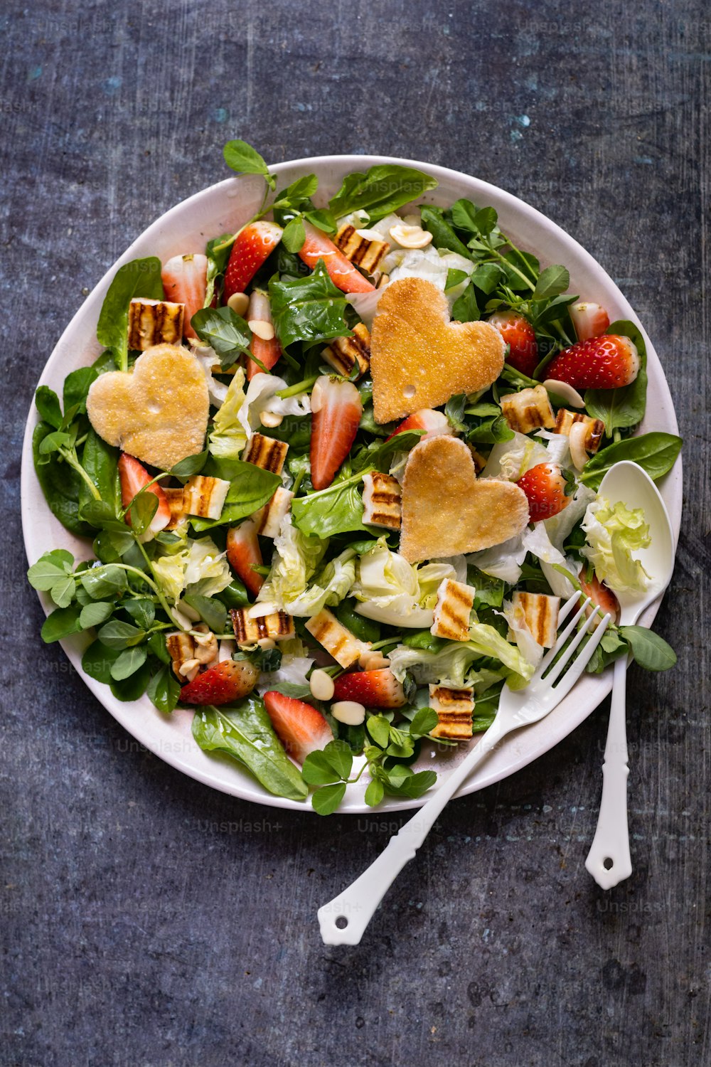 a plate of salad with strawberries and heart shaped croutons